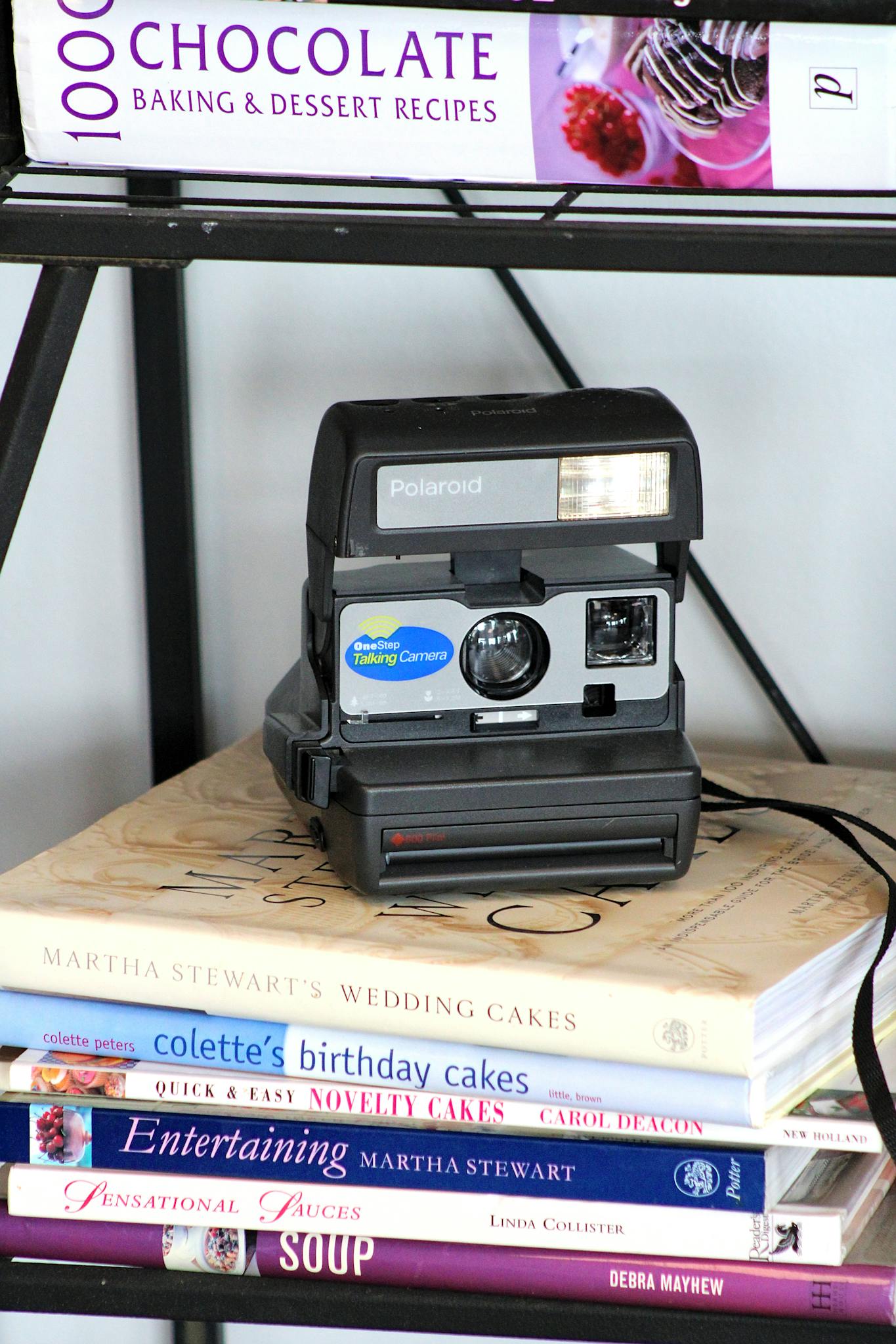 Vintage Polaroid camera placed on a stack of cookbooks, showcasing retro charm.