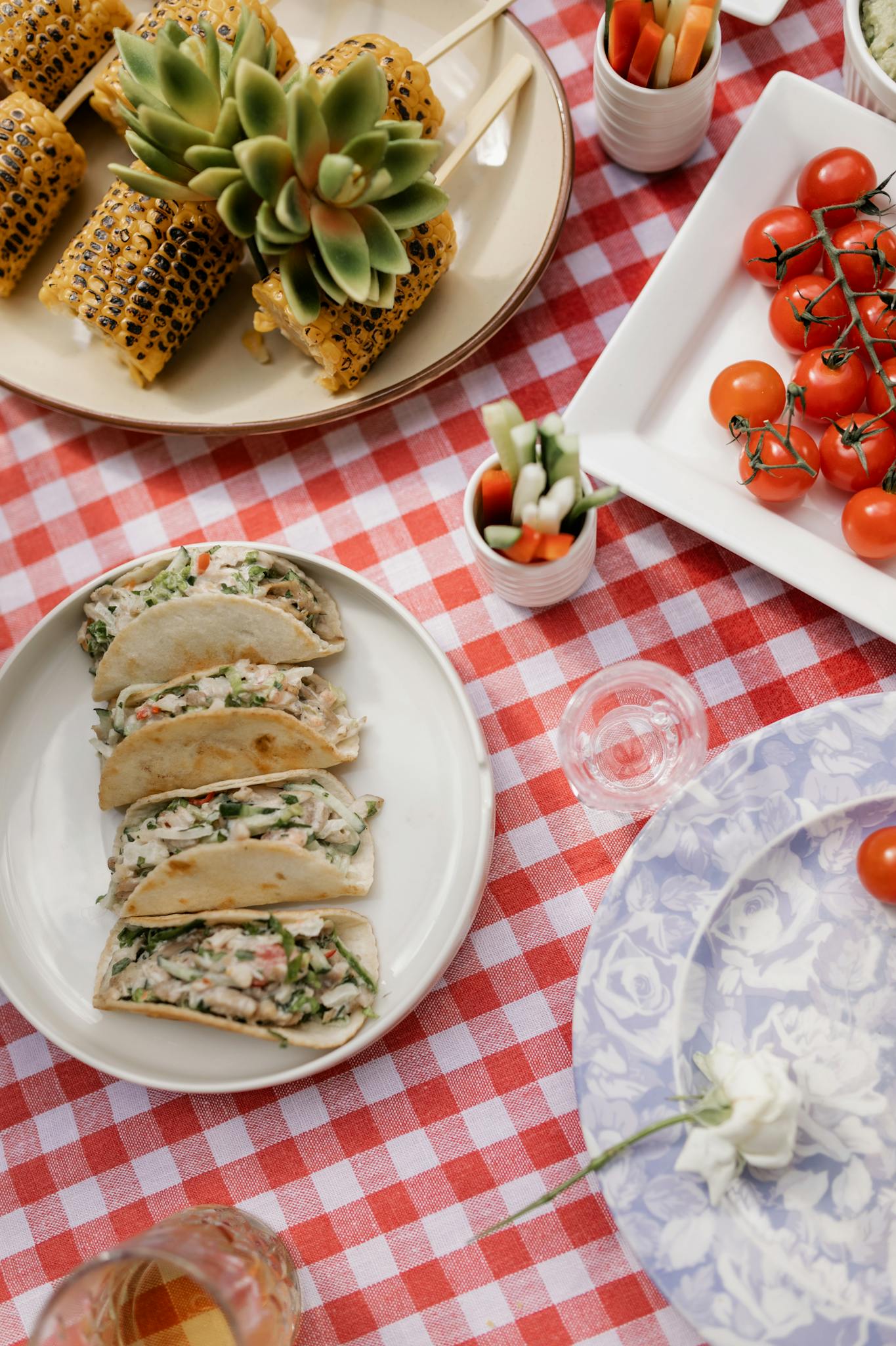 Charming outdoor picnic featuring tacos, grilled corn, and vibrant cherry tomatoes on a checkered tablecloth.