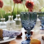 Chic outdoor table scene with blue glass surrounded by flowers and fruit.