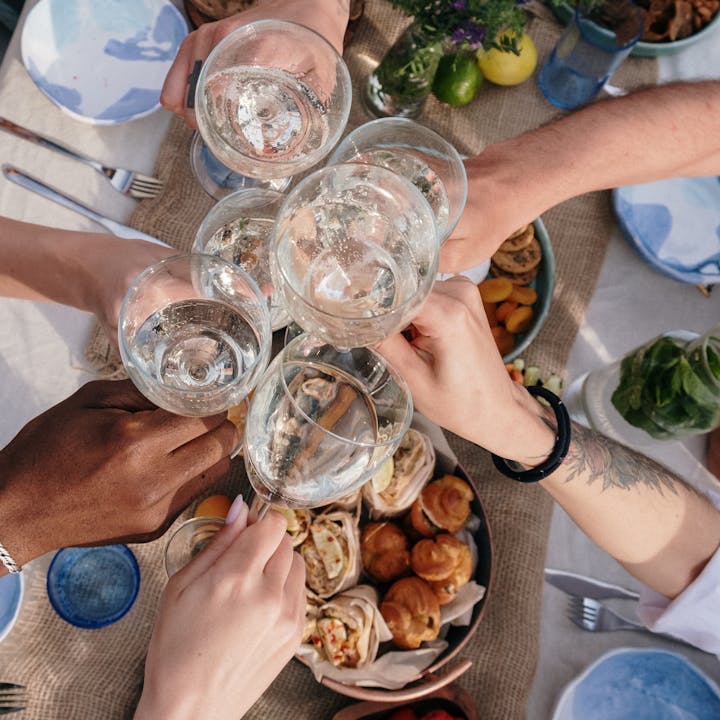 A cheerful group clinks glasses during an outdoor brunch celebration, with diverse hands and appetizing food.