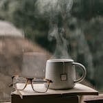 Comforting setup with books, glasses, and hot tea by a rain-drenched window, perfect for reading.