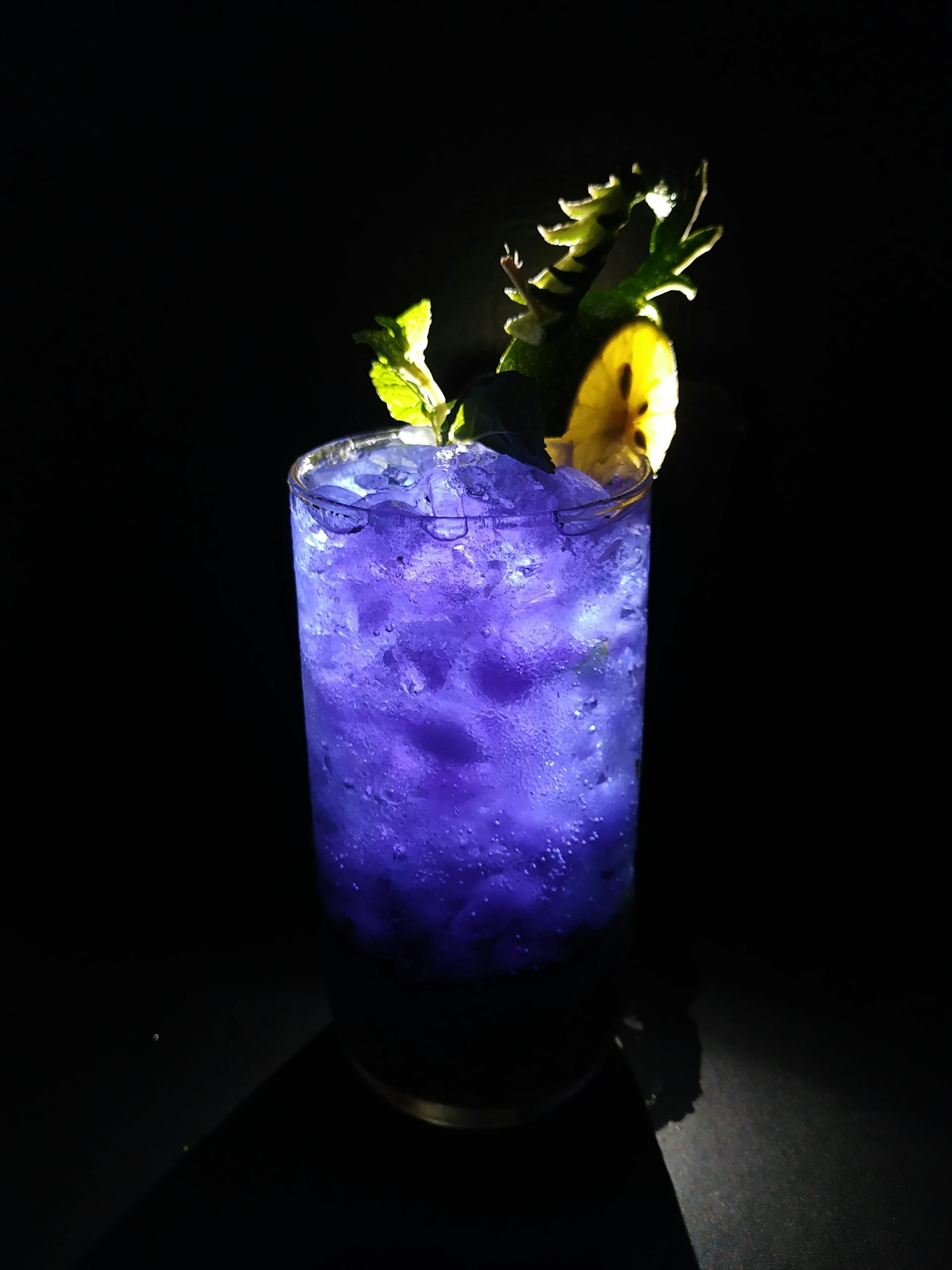Refreshing blue mocktail with ice and pineapple garnish on black background.