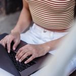 Crop unrecognizable female browsing internet on modern netbook while sitting on street near blurred railing during online work in city