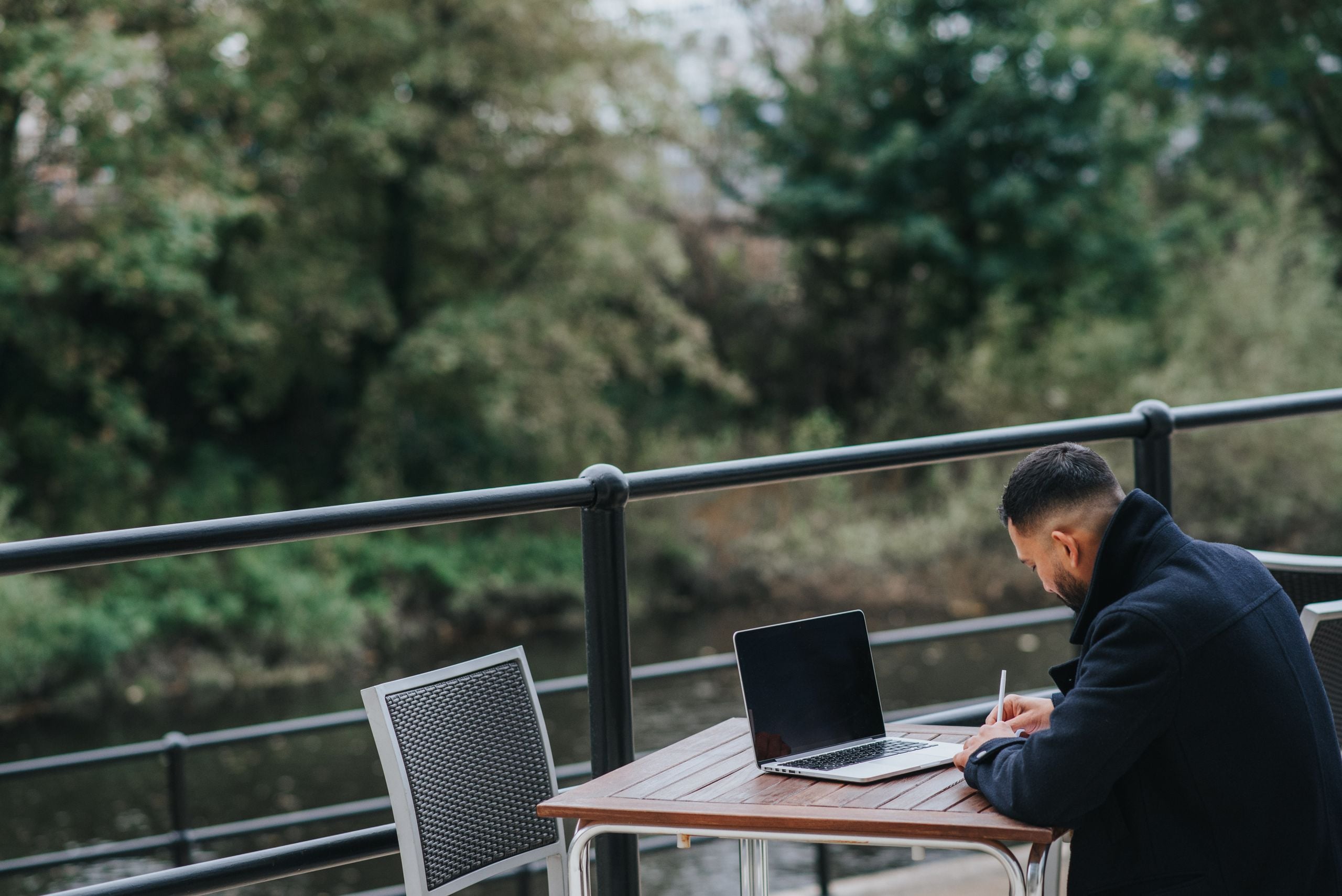 Side view of unrecognizable ethnic male executive taking notes near netbook at cafeteria table on veranda